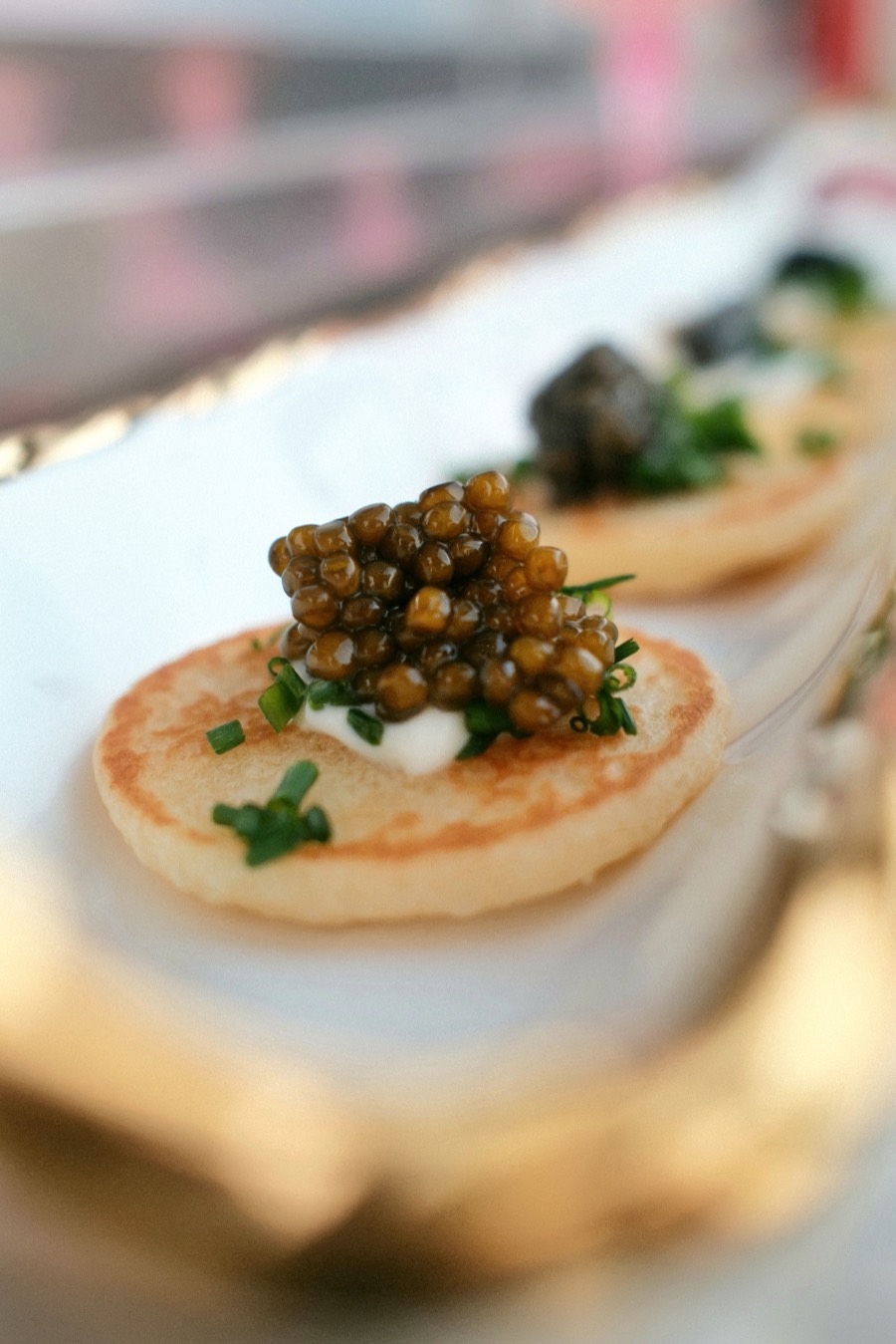 Warm blini with crème fraîche, caviar and chive on a gold-rimmed tray