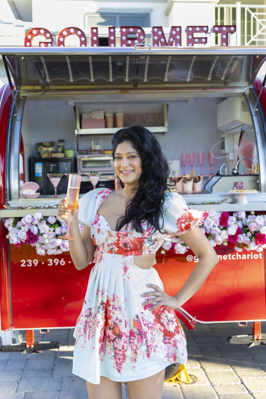 Nisha Singh, founder of Gourmet Chariot, in front of the Chariot with a glass of champagne